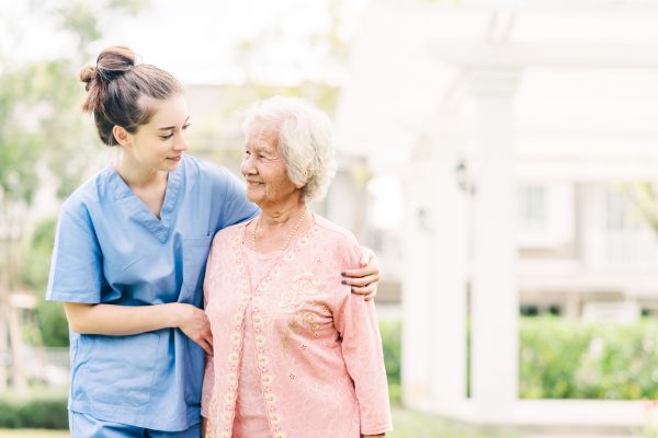 Smiling nurse caregiver with Asian elderly woman outdoor in the park